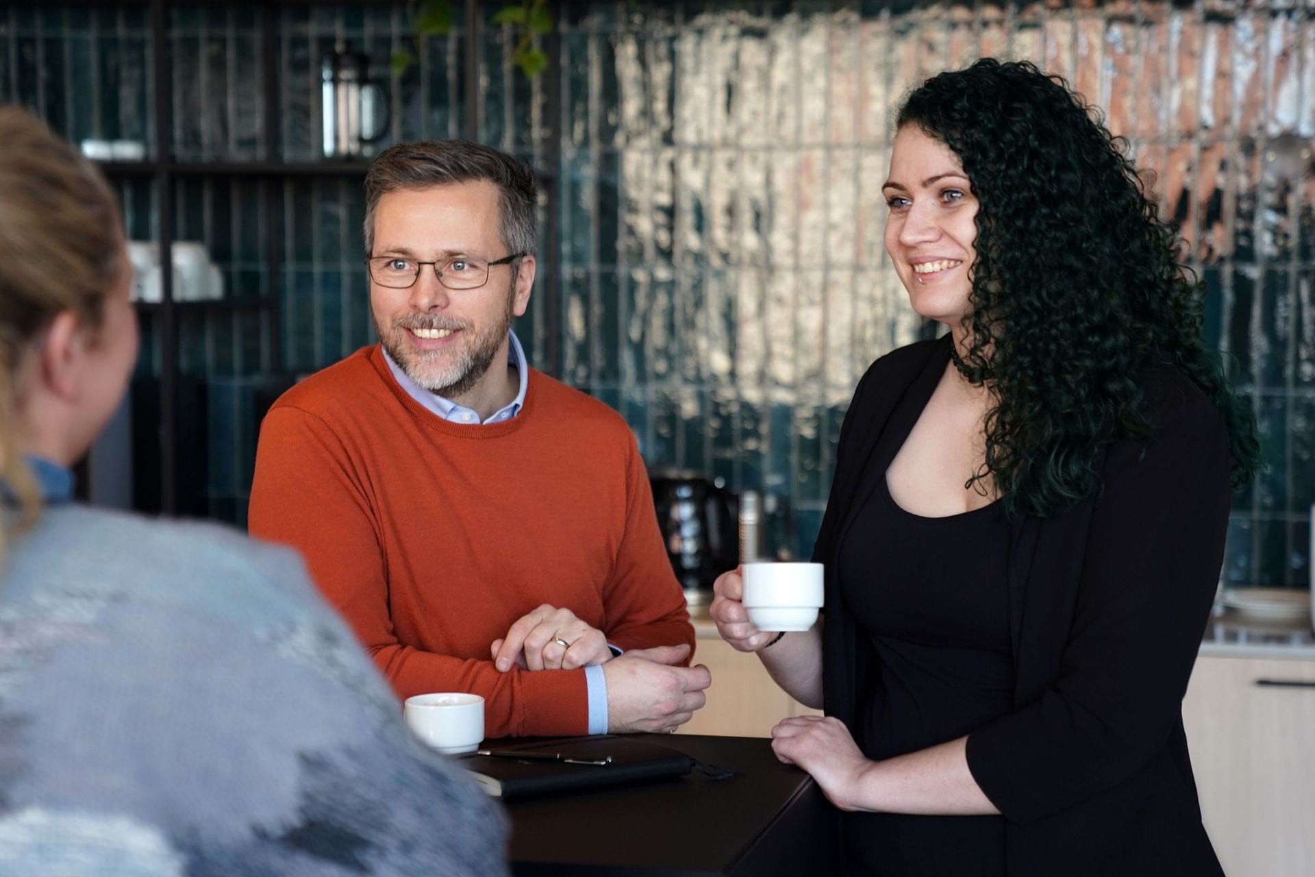 Kona og maður með kaffibolla brosa og tala saman